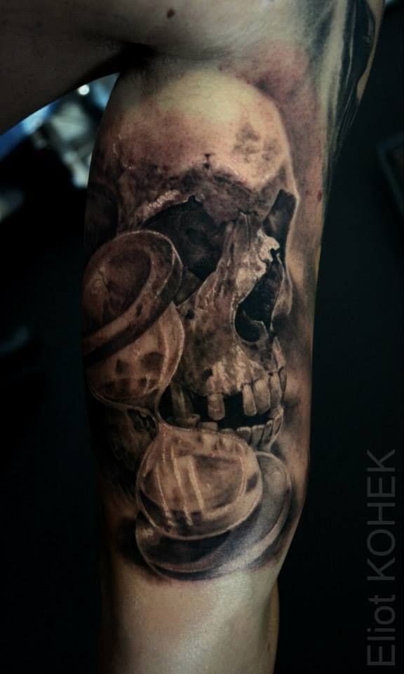 Tatuaje de bíceps detallado de estilo 3D de cráneo humano con reloj de arena de Eliot Kohek