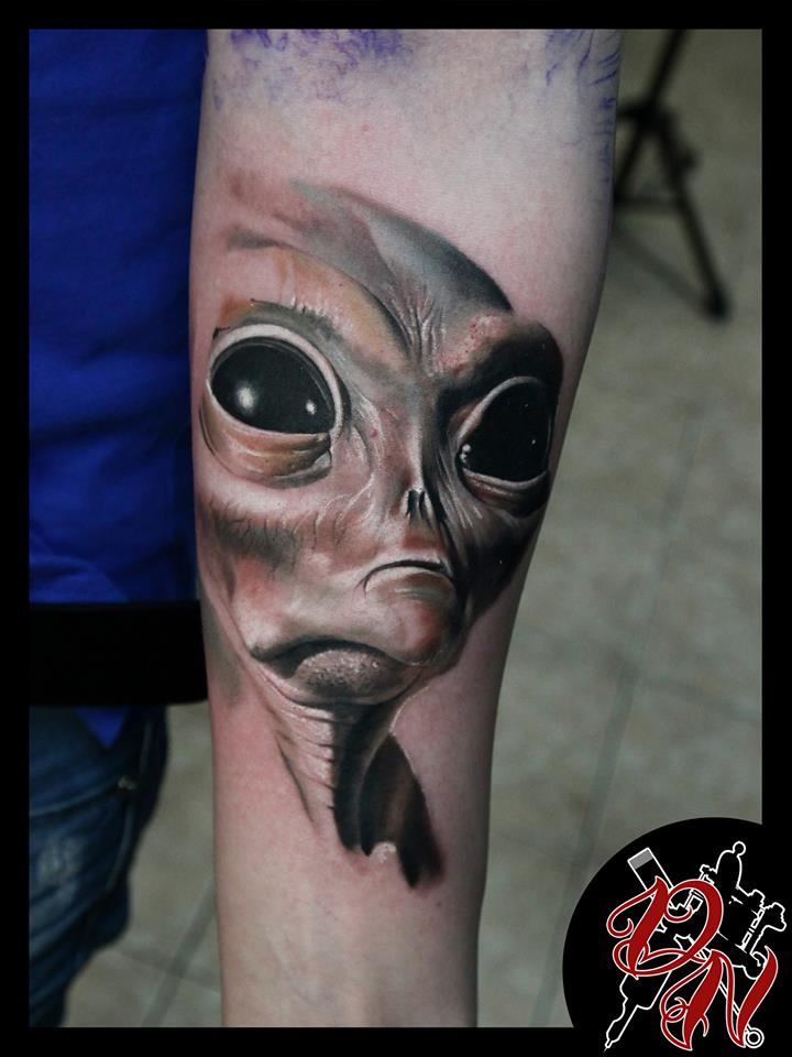 Alien face tattoo on arm
