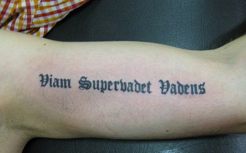 Black gothic-lettered quote tattoo on arm