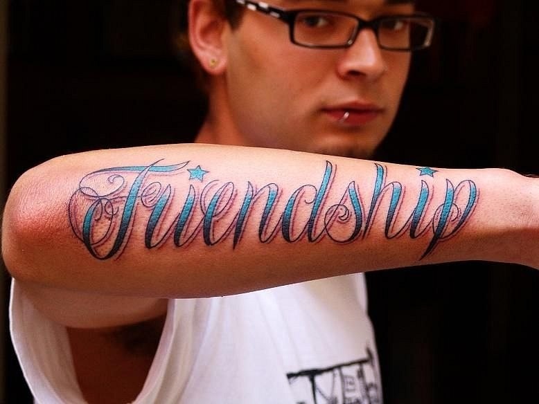Blue-lettered frendship quote tattoo on arm