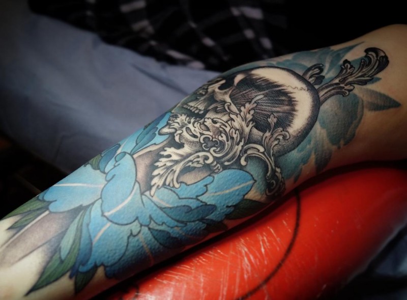 Blue flower and black skull tattoo on arm