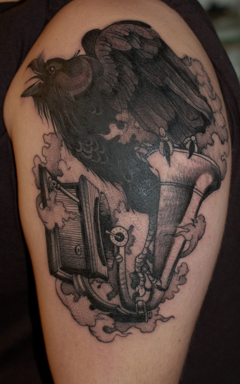 Cartoon black-and-white raven with gramophone in clouds tattoo on upper arm