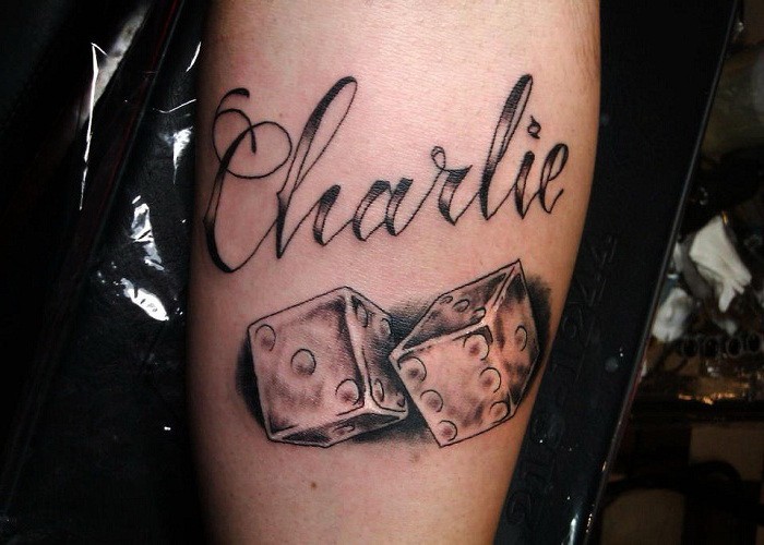 Tattoo mit Spielwürfeln und Aufschrift &quotCharlie" am Arm