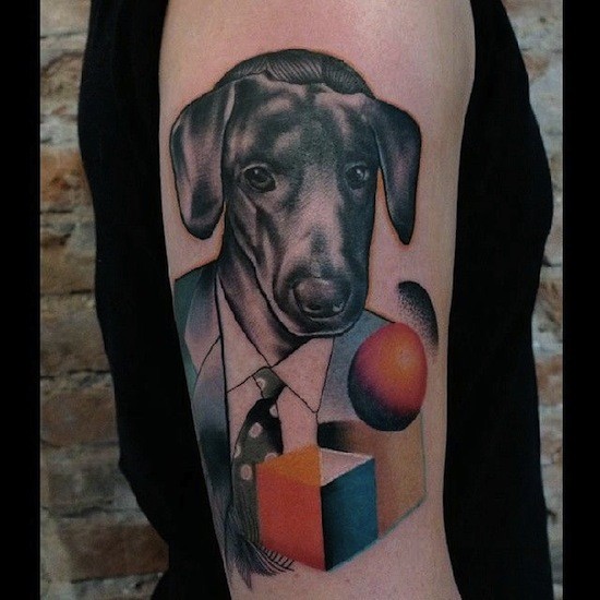 Colored designed by Mariusz Trubisz upper arm tattoo of human with dog head and geometrical figures
