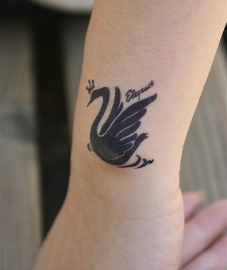 Cute black-ink swan with crown and quote tattoo on arm