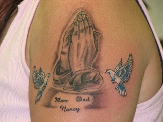 Tattoo mit süßen Tauben, betenden Händen und Aufschrift am Oberarm