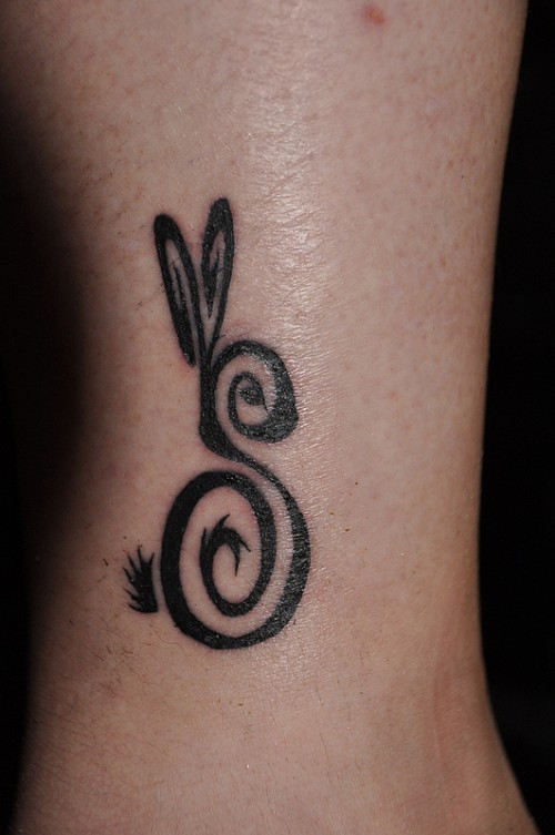 Cute uncolored curled hare tattoo on leg