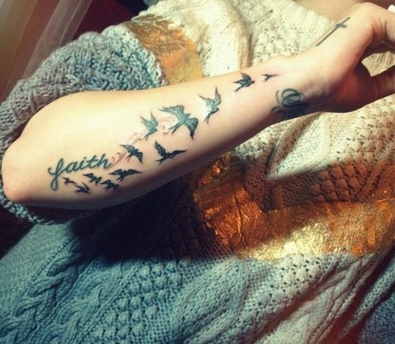 Tatuaje en el antebrazo, bandada de aves y palabra fe