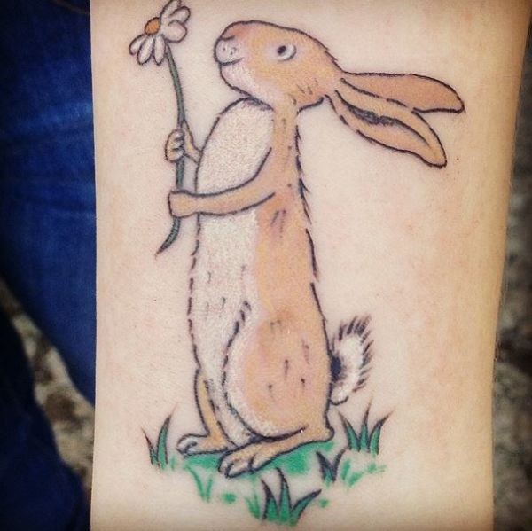 Funny cartoon colorful hare hanging camomile tattoo on arm