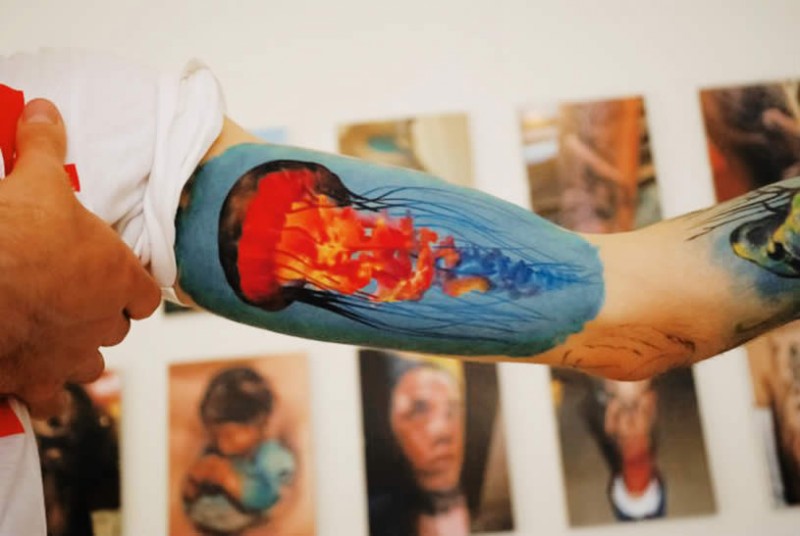 Gorgeous colored jellyfish on blue background tattoo on upper arm