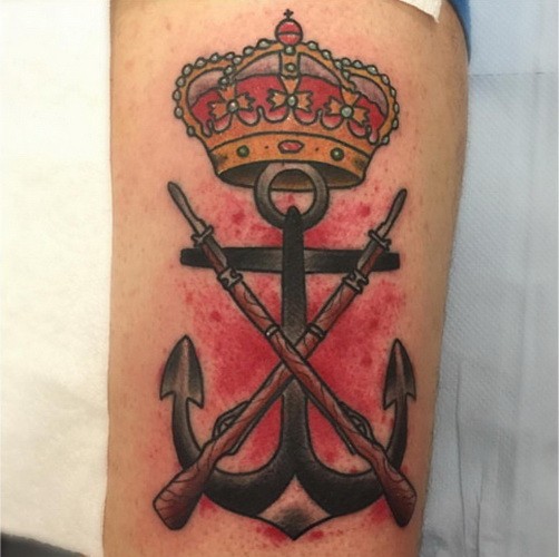 Harsh iron anchor with crown and guns on bloody background tattoo on forearm