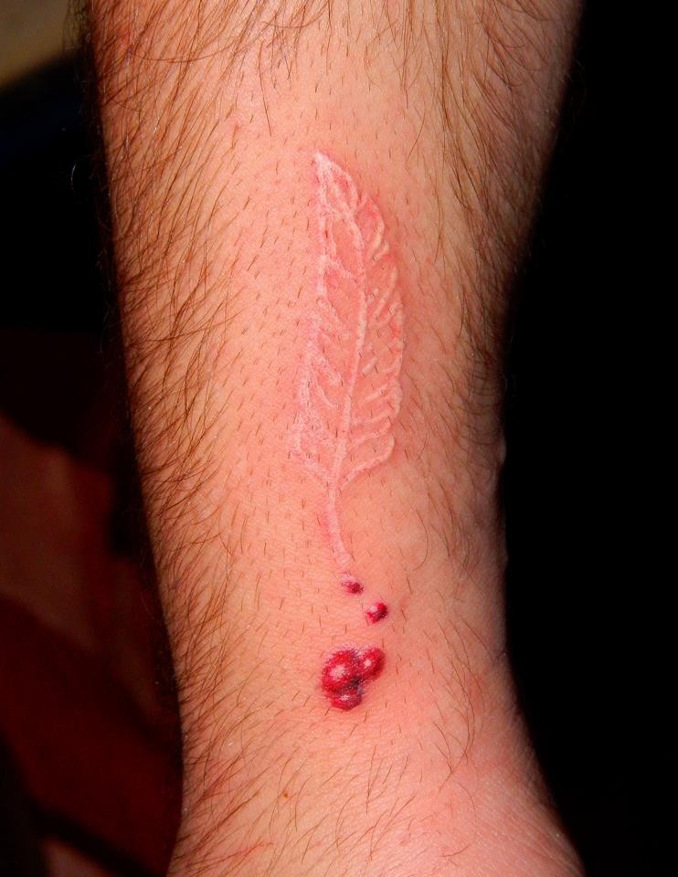 Lange weiße Feder mit roten Tropfen Tattoo am Arm