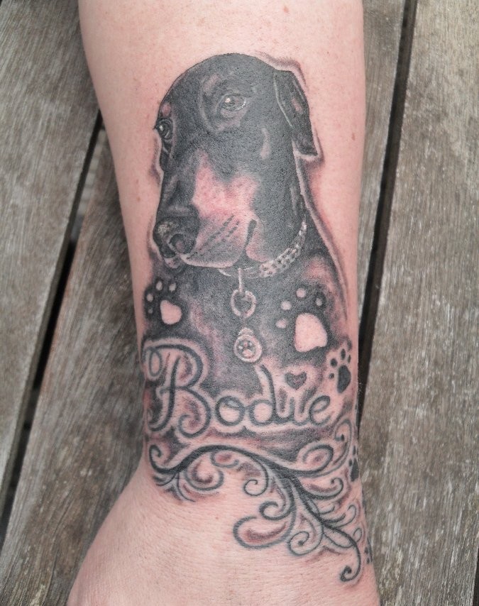 Arm Tattoo mit süßem  Dobermann in Schwarzweiß und Inschrift mit Namen
