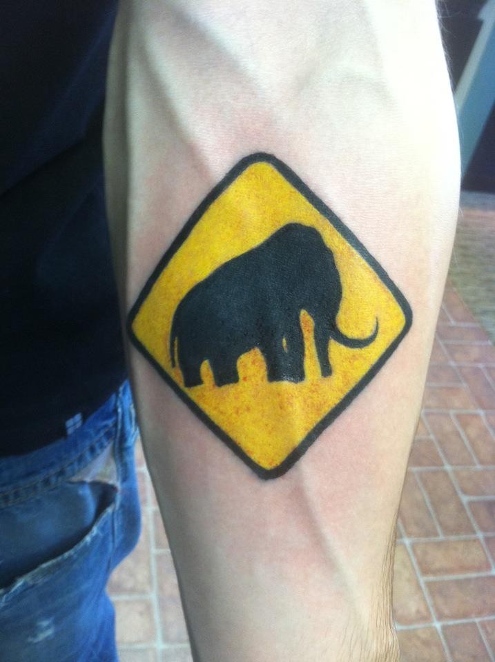 Tatuaje en el antebrazo, signo de mamut, colores amarillo y negro