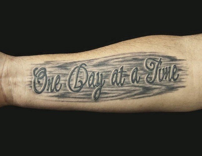 One day at a time quote on black background tattoo on arm