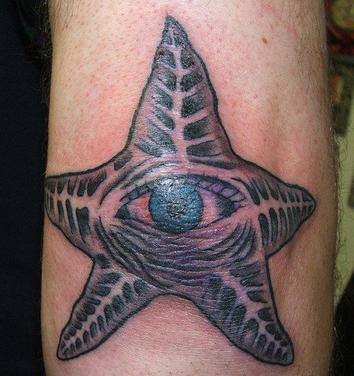Scary black-ink starfish with blue eye tattoo on arm