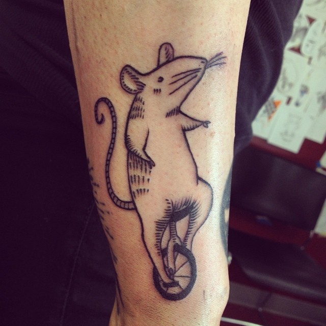 Simple uncolored rodent on unicycle tattoo on arm