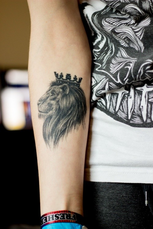 Small black-and-white lion king in crown tattoo on forearm