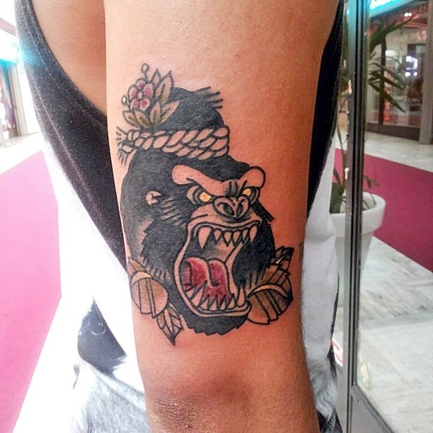 Small dreadful gorilla head in hat tattoo on upper arm
