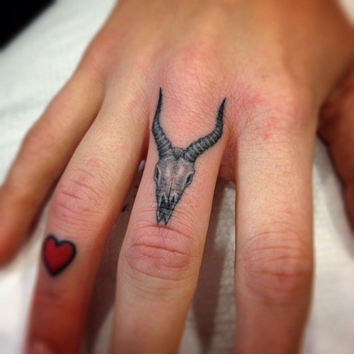 piccolo realistico nero e bianco teschio di capra cornuto  e cuore tatuaggio sulle  dita