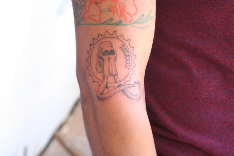 Arm Tattoo mit kleinem nicht farbigem Mammutschädel in der Sonne mit arabischen Zahlen