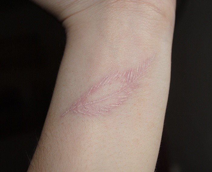 Tender white-contour feather tattoo on wrist