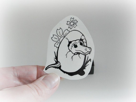 Tiny reptile hatching from egg with flowers tattoo design