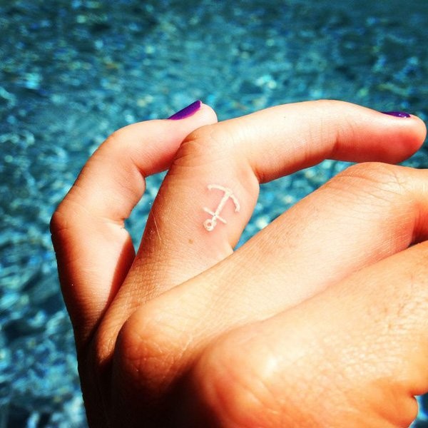 Tiny white-ink anchor tattoo on ring finger