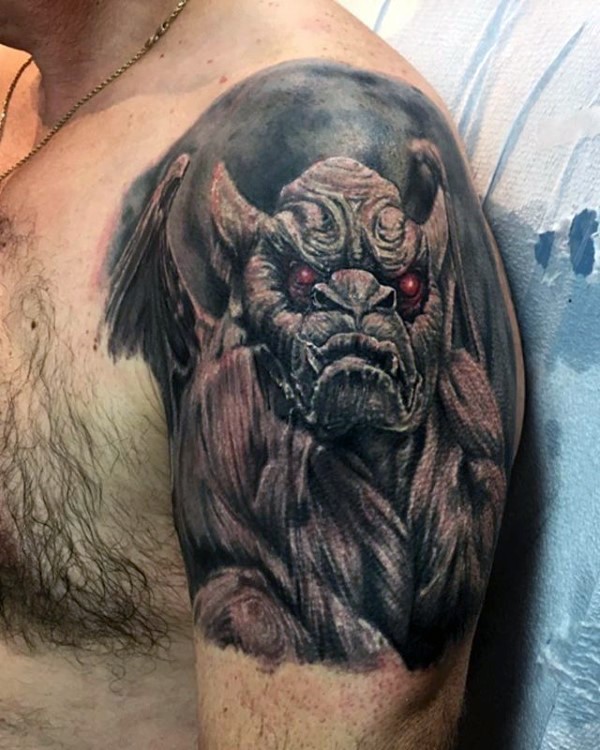 Very realistic looking colored gargoyle with red eyes tattoo on upper arm