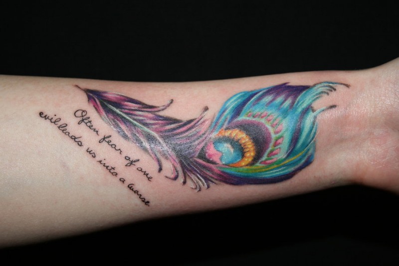 Vivid-colored peacock feather with quote tattoo on forearm