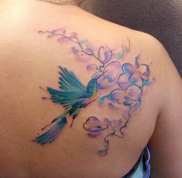 Tatuaje en el omóplato,  pájaro azul gracioso  con flores, colores suaves