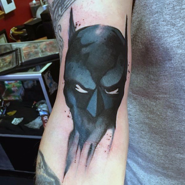 Abstract style black ink Batman mask like tattoo on arm