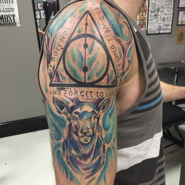 Abstract style illustrative colored shoulder tattoo of deer with Harry Potter movie symbol and lettering