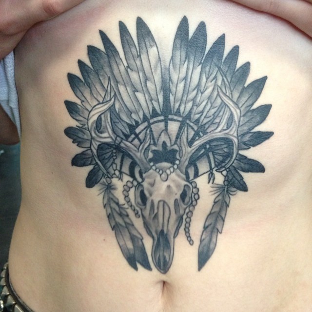 Accurate designed big colored Indian style animal skull tattoo on belly stylized with helmet from bird feather