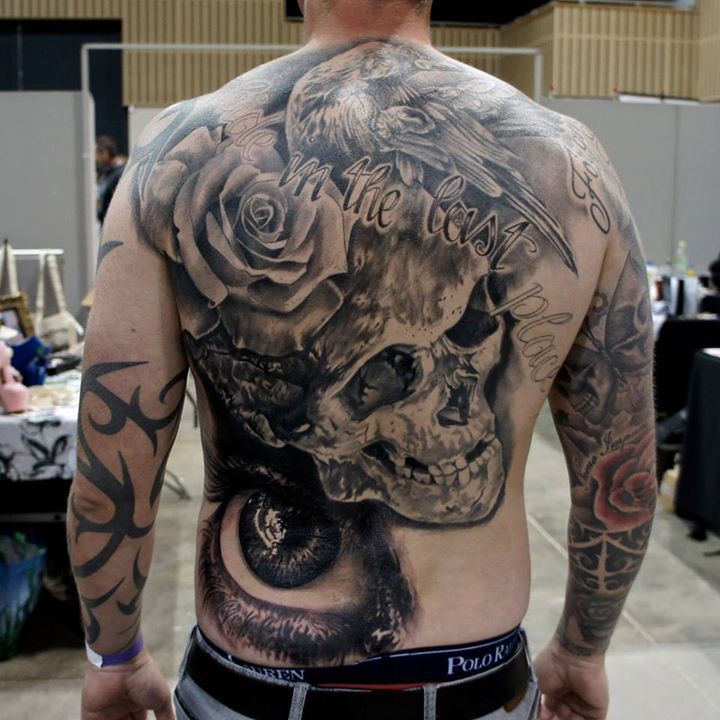 Amazing detailed black ink human skull tattoo on back with eagle, lettering and flower