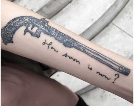 Tatuaje en el antebrazo, arma de fuego y inscripción