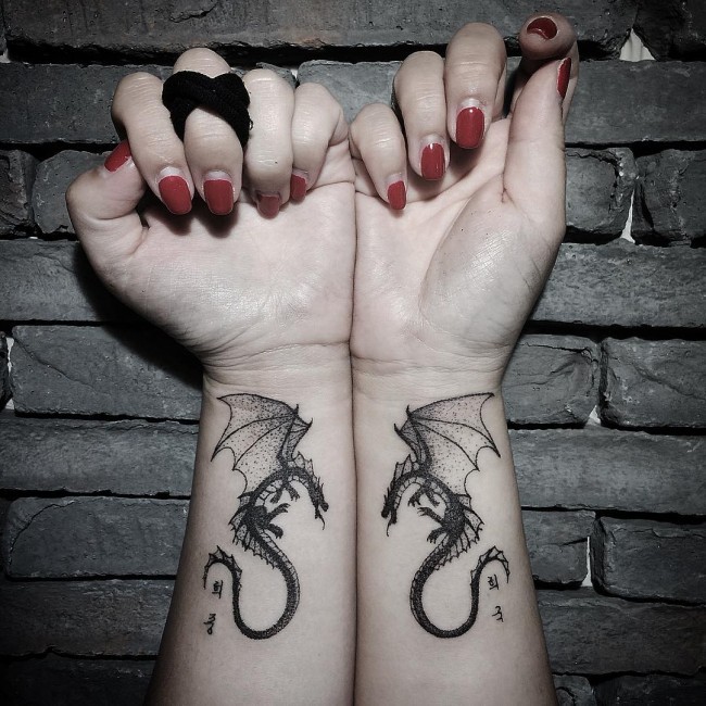 Tatuajes de dragones semejantes  en dos muñecas, tinta negra