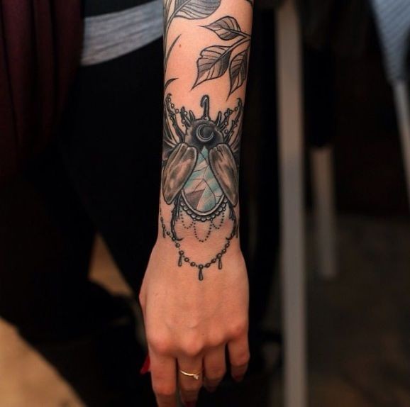 Tatuaje en la muñeca, escarabajo con joya y hojas