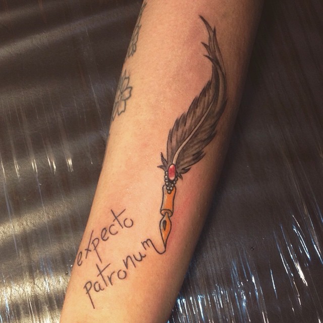 Awesome fantasy style colored feather shaped pen tattoo on forearm with lettering