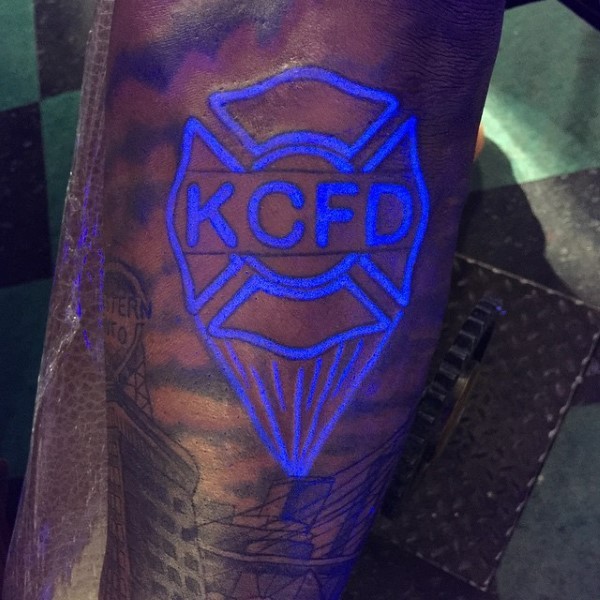 Awesome glowing ink like painted blue emblem with lettering tattoo on arm