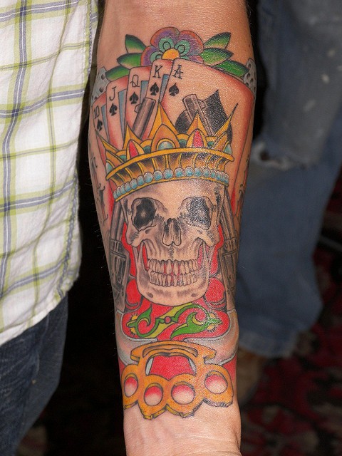 Erschütterndes Tattoo von Totenkopf mit Spielkarten und Schlagring als König gestaltet am Unterarm