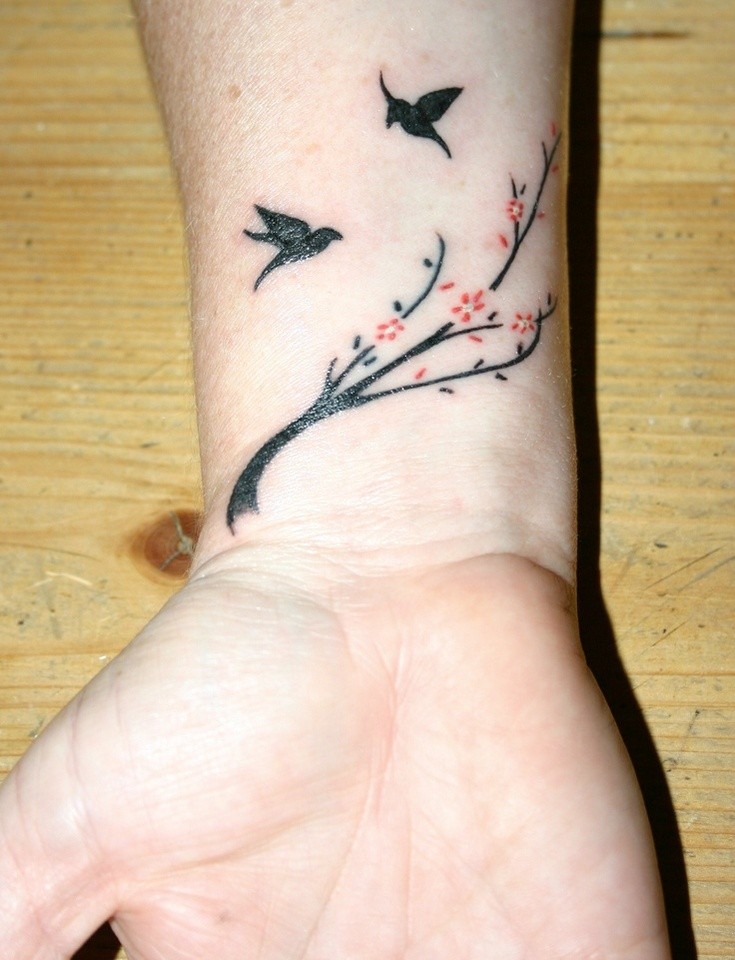 Tatuaje en la muñeca,
dos aves negras y  ramita con flores