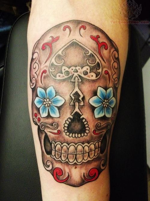 Tatuaje en el antebrazo, calavera de azúcar con dos flores azules