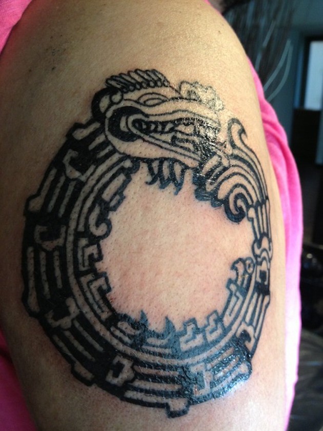 Aztec dark black circle shaped stylized dragon upper arm tattoo