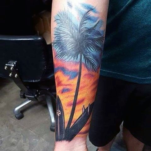 Beautiful colored lonely palm tree with surfing boards tattoo on arm