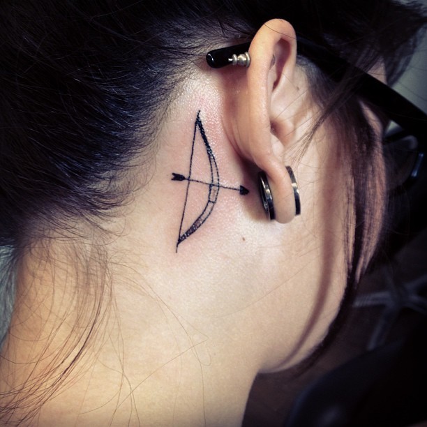 Tatuaje de arco y flecha detrás de la oreja