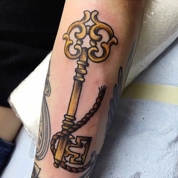 Tatuaje en el antebrazo, llave dorada  antigua larga con cuerda