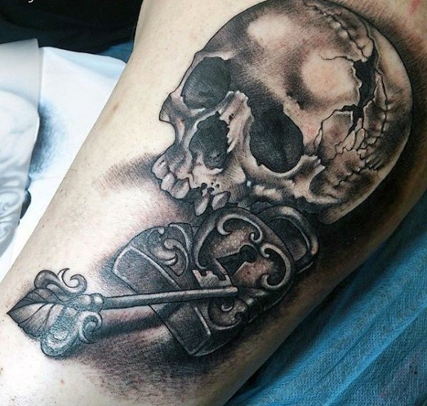 Tatuaje en el brazo, cráneo agrietado y llave con  candado  colores negro blanco