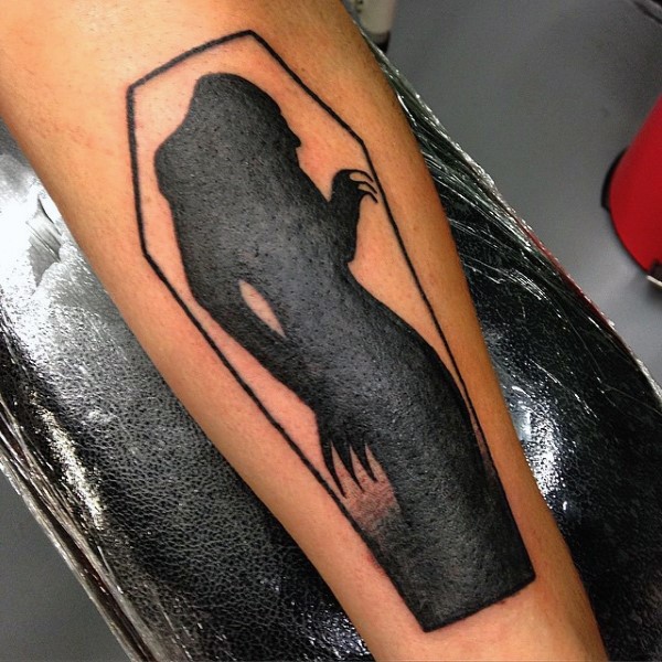 Tatuaje en el antebrazo, silueta negra de mujer monstruosa en el ataúd