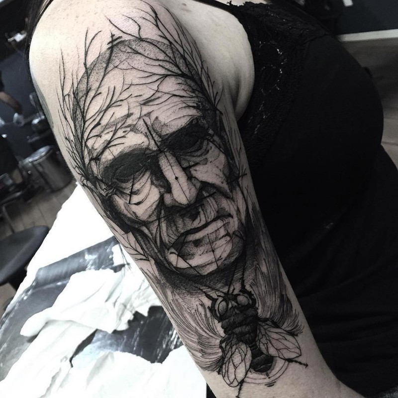 BIg black ink mystical old man face tattoo on shoulder combined with fly